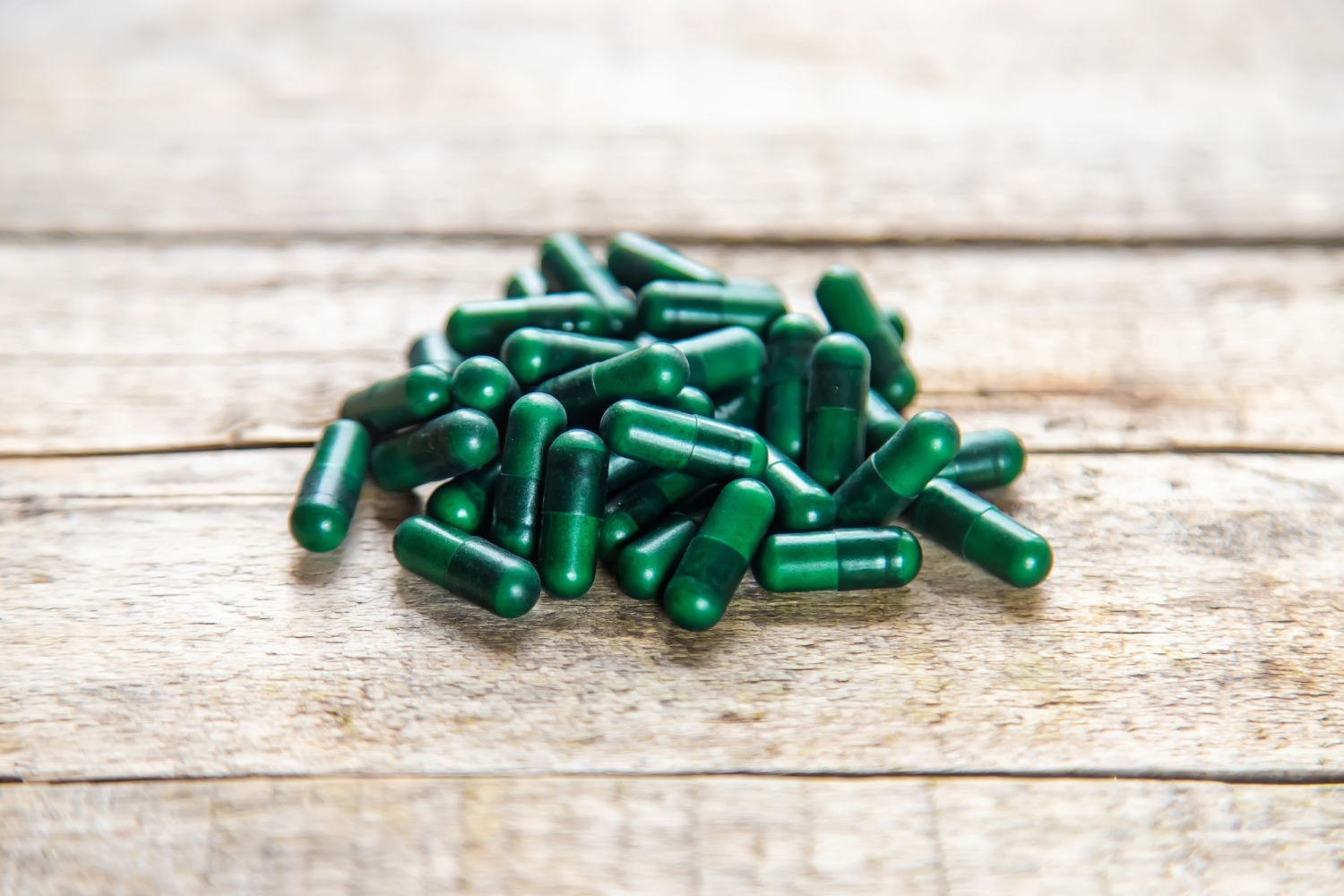Capsules vertes contenant de la spiruline posées sur une table en bois